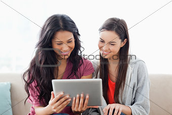 A woman with her friend smiling as they both look at the tablet 