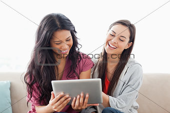 A laughing pair of women on the couch watching their tablet pc 