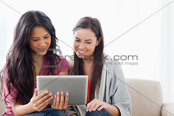 A woman holding a tablet with her friend on the couch as they wa