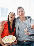 A laughing couple sitting on the couch with popcorn as they watc
