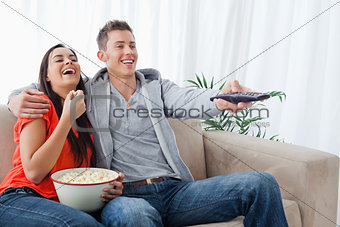 A laughing couple enjoying a tv show together as they hold each 