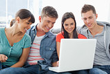 A smiling group of friends sitting around a laptop