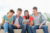 A group of friends sit on the couch while watching a tablet pc
