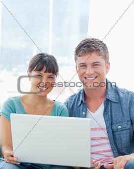 A smiling couple with a laptop as they look into the camera