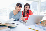Two girls smiling as they use the laptop as one girl points at s