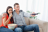 A couple sitting together embracing as they watch tv and eat pop