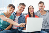 A group of smiling friends gathered around a laptop 
