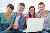 A smiling group of friends sitting together with a laptop as the