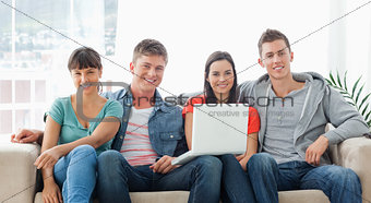 A group of friends sit on the couch with a laptop as they look a