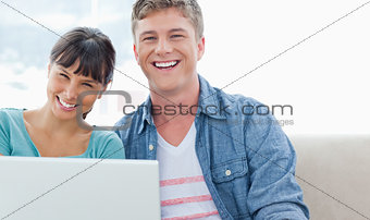 A laughing couple sitting on the couch with a laptop as they loo