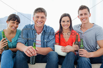 A smiling group sitting on the couch while holding beers 