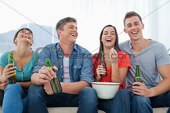 Laughing group of friends sitting with beers in their hands and 