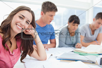 A girl smiling at the camera with her friends beside her studyin