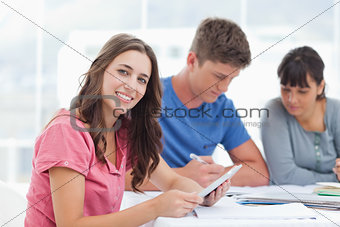 A brightly smiling girl with friends as she uses a tablet