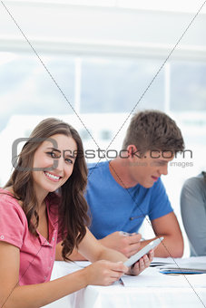 A smiling girl sits and uses her tablet pc with friends near her