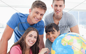 A smiling group of people looking into the camera with a globe b