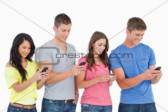 Four friends standing to the side slightly sending texts
