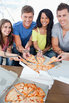 Smiling friends taking some pizza as they look at the camera
