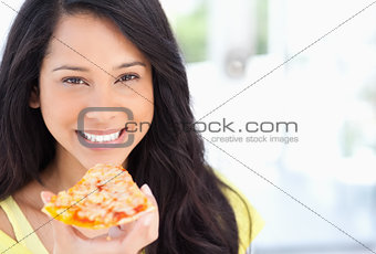 A smiling woman holding a slice of pizza as she looks at the cam