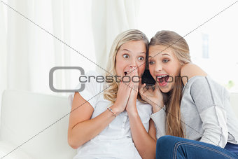 A shocked and happy pair of girls making a phone call