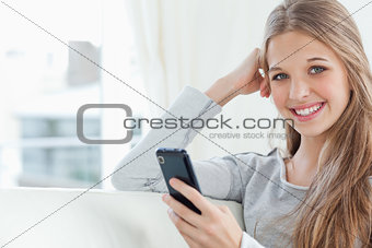 A smiling girl with a phone in hand as she looks at the camera 