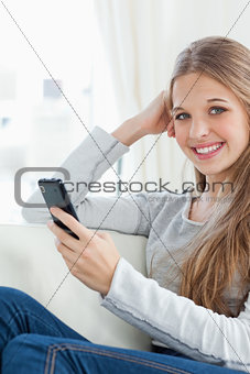 A smiling girl holds a phone in her hand as she looks at the cam