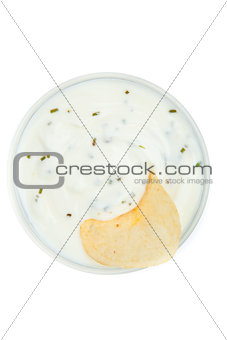 Close up of a bowl of white dip with herbs and a chips dipped in