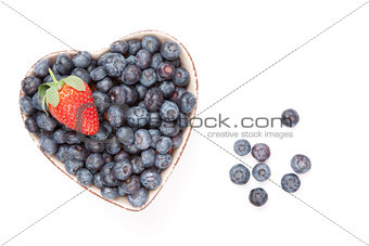 One strawberry and bluberries in  a heart shaped bowl