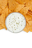 Close up of a bowl of dip with herbs surrounded by nachos