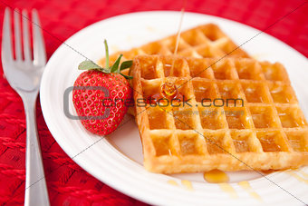 Waffles and syrup and strawberry together in a white plate