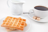 Waffles sugar milk and a cup of coffee on white plate with spoon