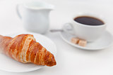 Croissant and a cup of coffee on white plates with sugar and mil