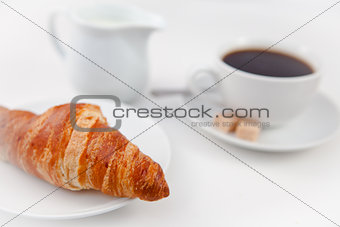 Croissant and a cup of coffee on white plates with sugar and mil