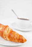 Croissant and a cup of coffee with a spoon on white plates