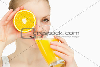 Woman placing an orange on her eye while drinking
