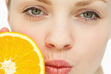 Close up of a woman placing an orange near her mouth