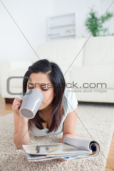 Woman drinking from a mug while holding a magazine