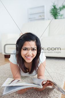Woman laying on the floor and smiles as she holds a magazine