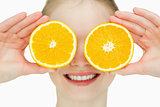 Close up of a cheerful woman placing oranges on her eyes