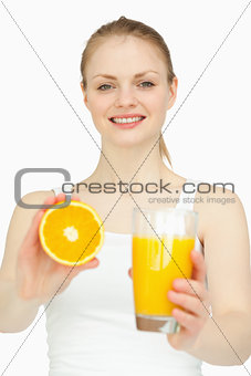 Smiling woman holding a glass while presenting an orange