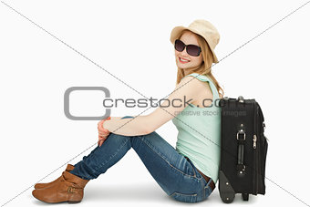Woman wearing sunglasses while sitting near a suitcase