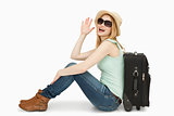 Woman raising her hand while sitting next to a suitcase