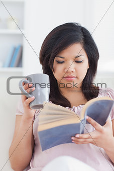 Woman holding a mug while reading a book