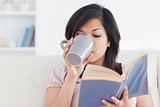Woman drinking from a mug while holding a book