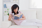 Woman lying on a sofa while holding a mug and a book