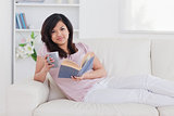 Woman lying on a couch while holding a mug and a book