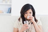 Sick woman blowing her nose while holding a glass of water
