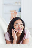 Smiling woman lying on a sofa while phoning