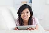 Woman smiling while resting on a couch and playing with a tablet