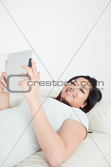Smiling woman lying on a sofa while holding a tactile tablet